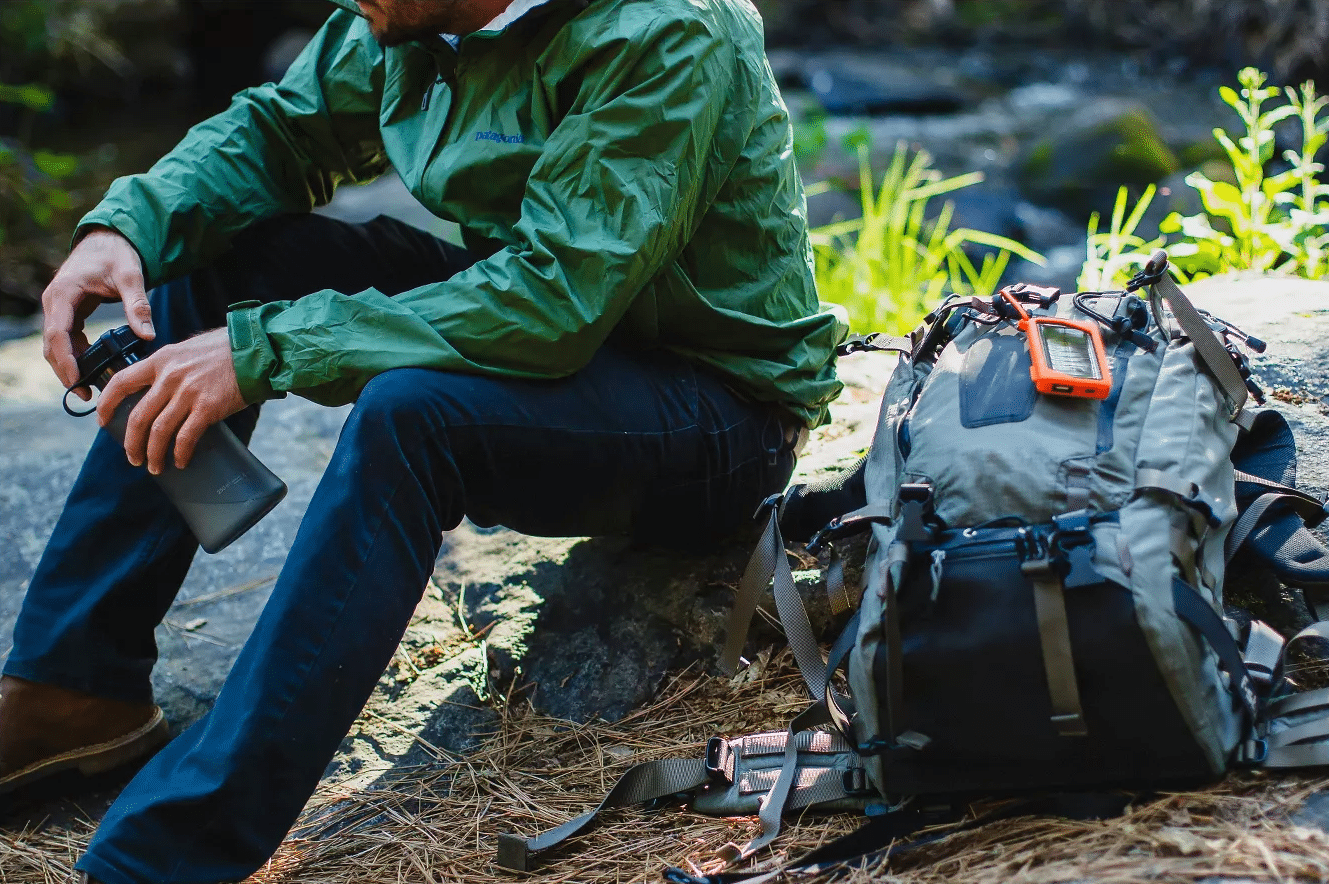 picture of the power bank in a outdoor environment. we see a hiker sitting down with the power bank hook to the back and charging with the sun light