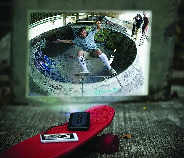 This image show our first design version of the portable projector for smartphone. the projector is on a skateboard, projecting youtube video from the skateboard to a wall in the street to share the footage captured earlier