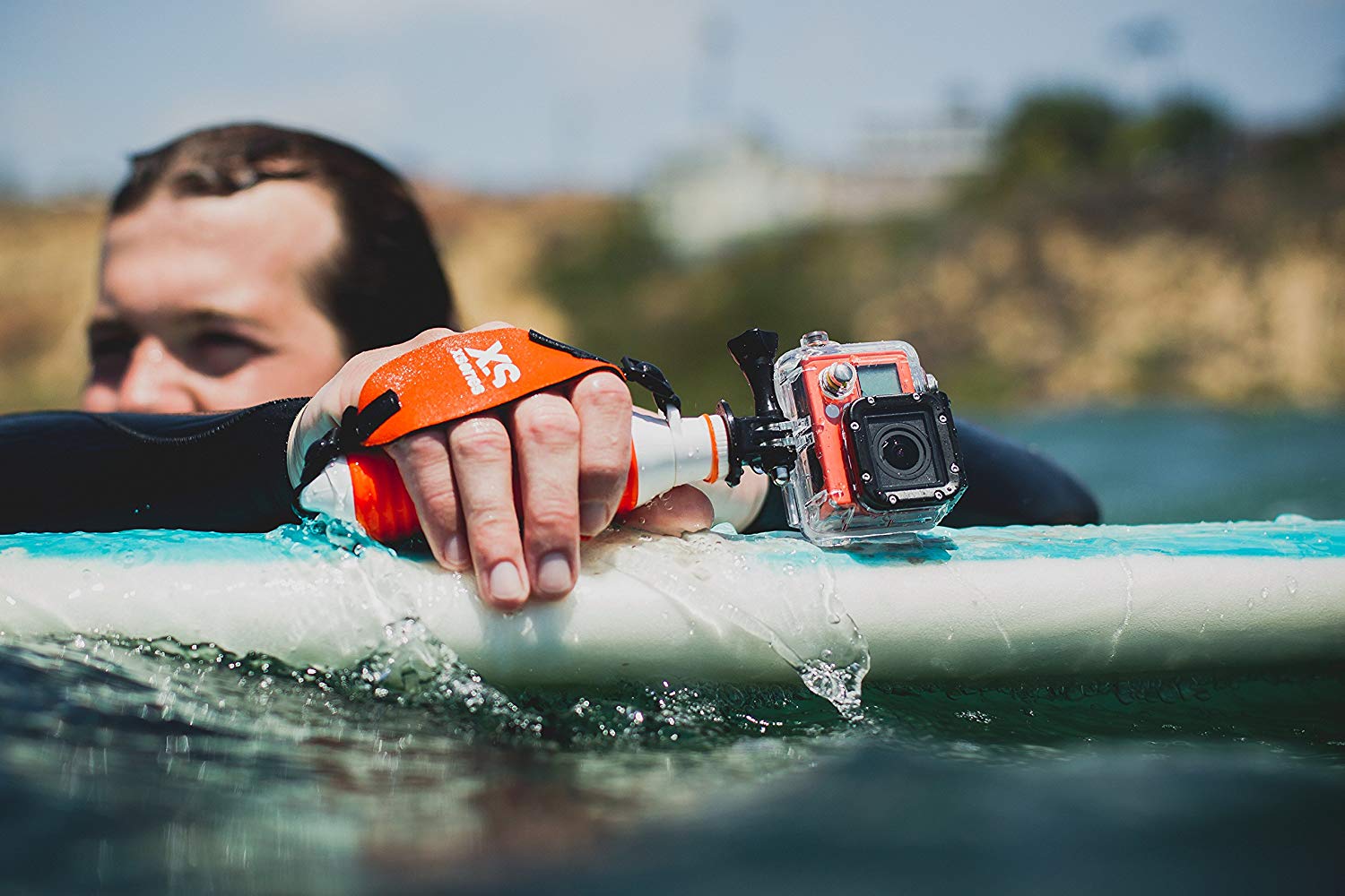 Our product in action with a GoPro black edition or a DJI Osmo Action camera. On the picture is a surfer in the water holding the surfboard and waiting waves. he is using our product, the U-Float, with the action camera that is floating on the surface of the water